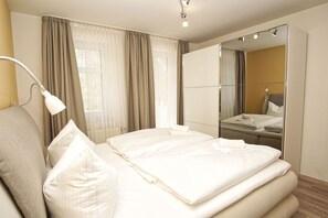 A hotel room with a bed, a mirror, a lamp, and a window with curtains. - Apartment Jasmund - Apartment in a central and quiet location - (Baabe)