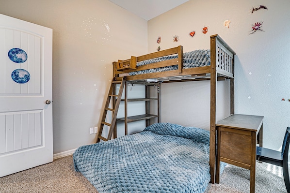 Una cama individual superpuesta con escalera, un escritorio y una silla en una habitación con puerta y decoración en la pared.