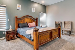 A bedroom with a wooden bed, a nightstand, two chairs, and a window with blinds.