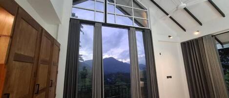A modern hotel room with a large sliding glass door, a bed, a ceiling fan, and a view of mountains.