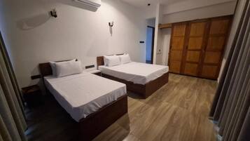 A hotel room with two beds, a ceiling fan, an air conditioning unit, and a wooden wardrobe.