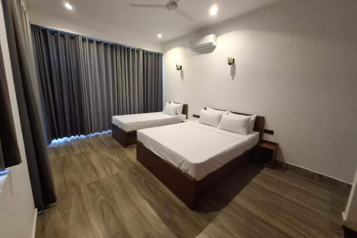 A hotel room with two beds, a ceiling fan, an air conditioning unit, and a curtain.