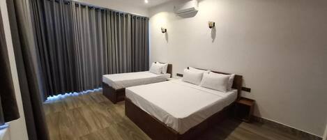 A hotel room with two beds, a ceiling fan, an air conditioning unit, and a curtain.