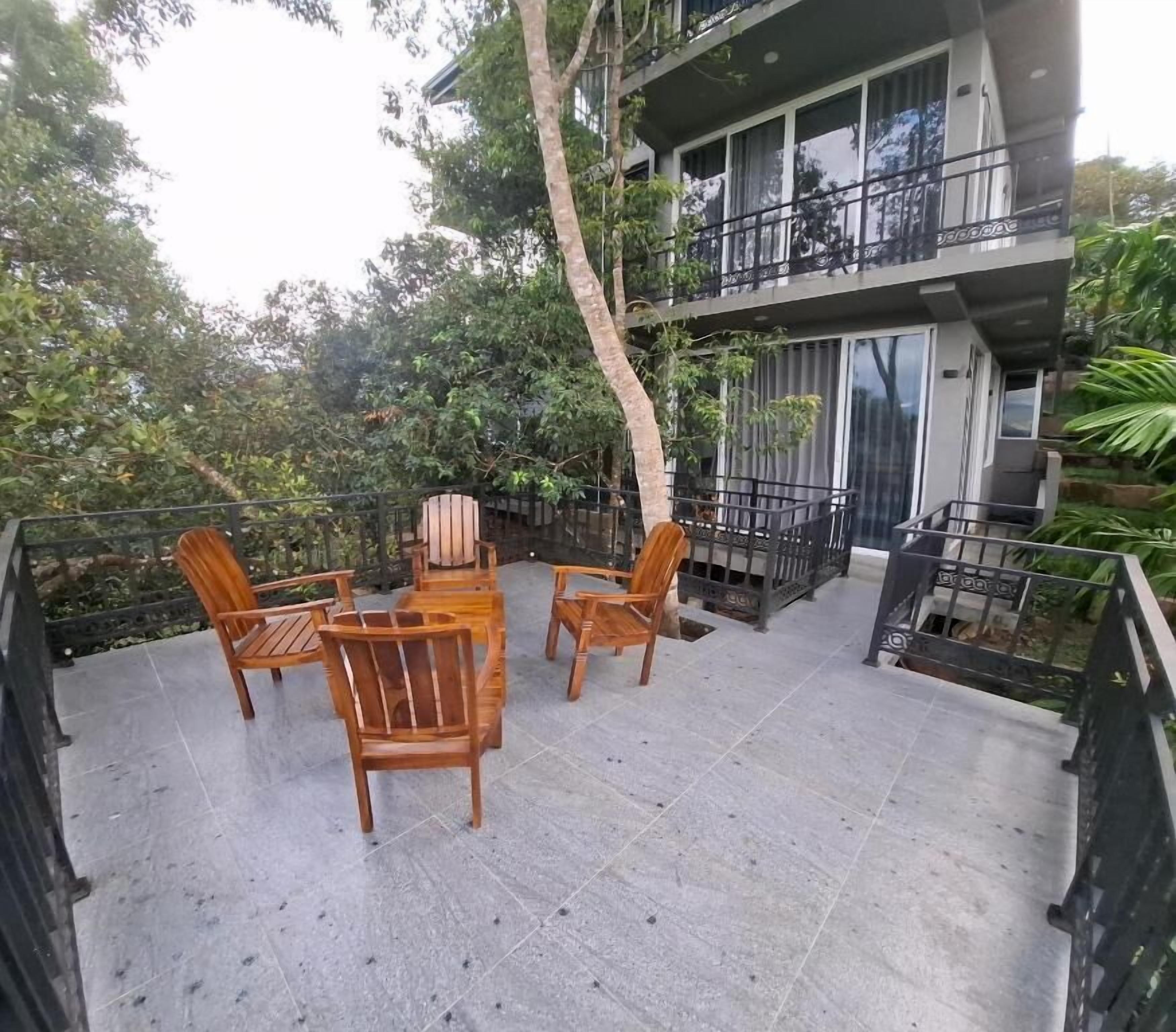 Une terrasse avec une table et des chaises, entourée d’arbres et bordée d’un immeuble doté de balcons.