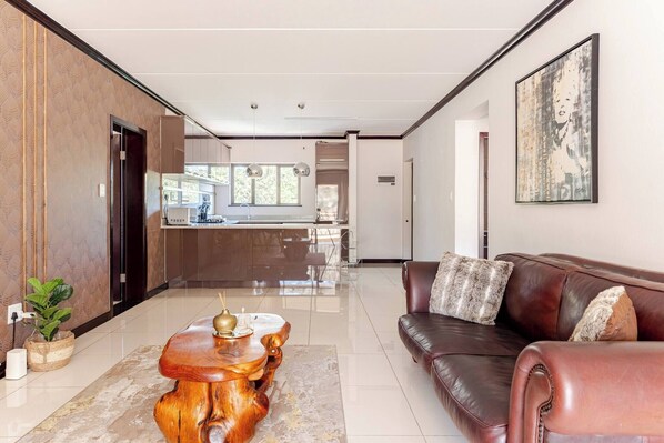 A modern living room with a leather sofa, a wooden coffee table, and a kitchen in the background.