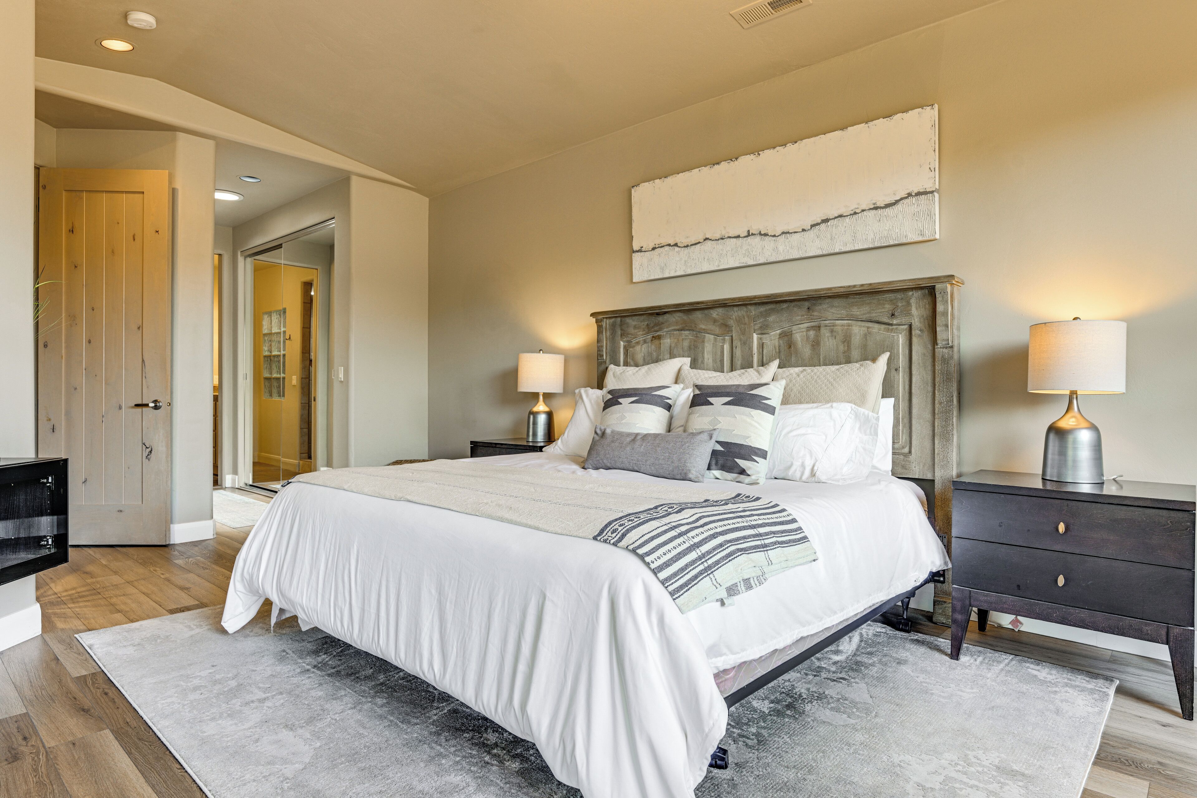 Une chambre à coucher avec un grand lit, des tables de chevet, une tête de lit en bois et une palette de couleurs neutres.