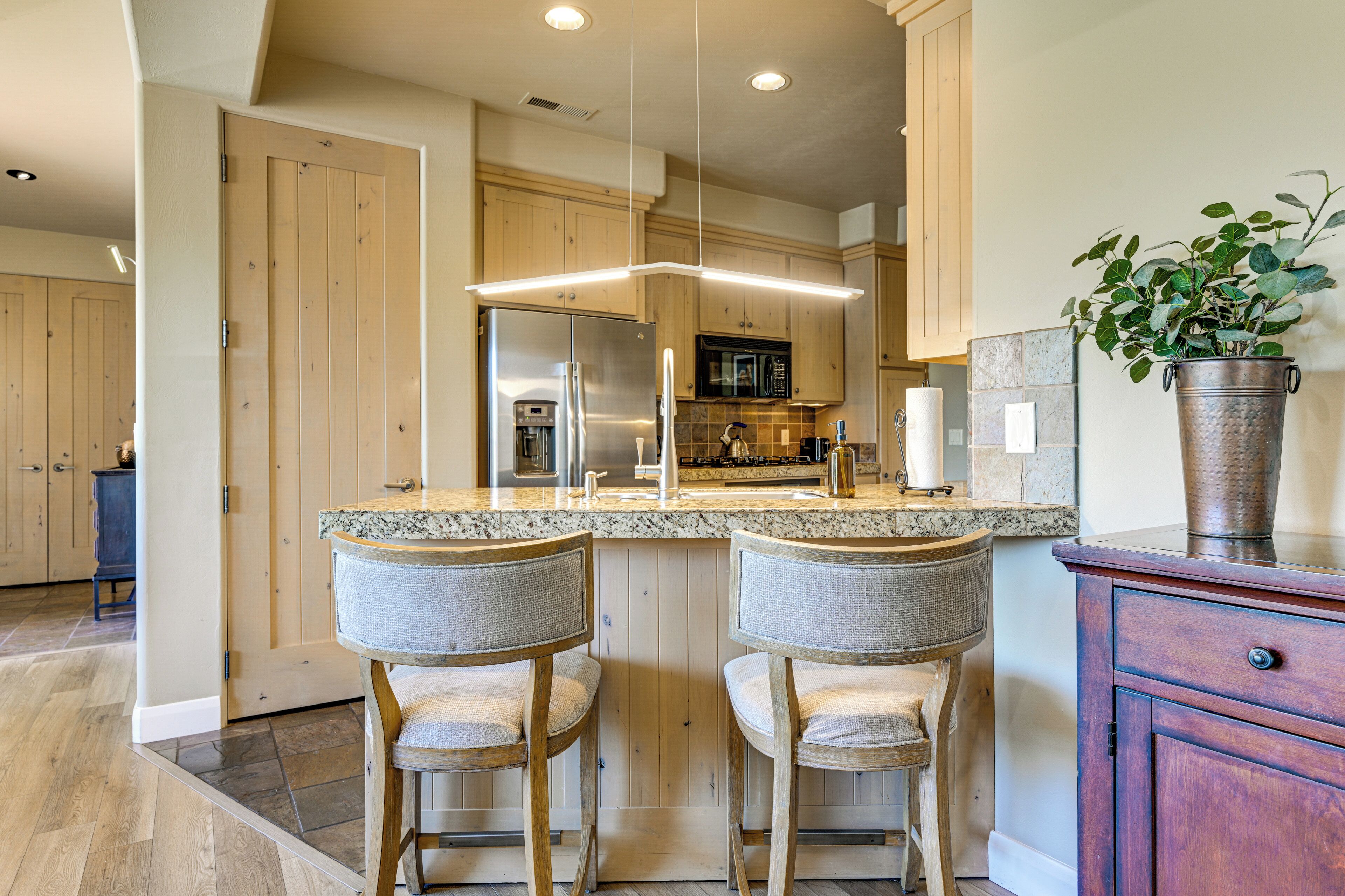 A kitchen with wooden cabinets, a stainless steel refrigerator, a microwave, and a granite countertop.