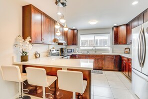 A modern kitchen with wooden cabinets, a large island with bar stools, stainless steel appliances, and a window providing natural light. - Walk to Sand! Ewa Beach Group Retreat (Ewa Beach)