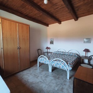 Une chambre à coucher comprenant un lit, une armoire, deux chaises, une petite table et deux lampes.