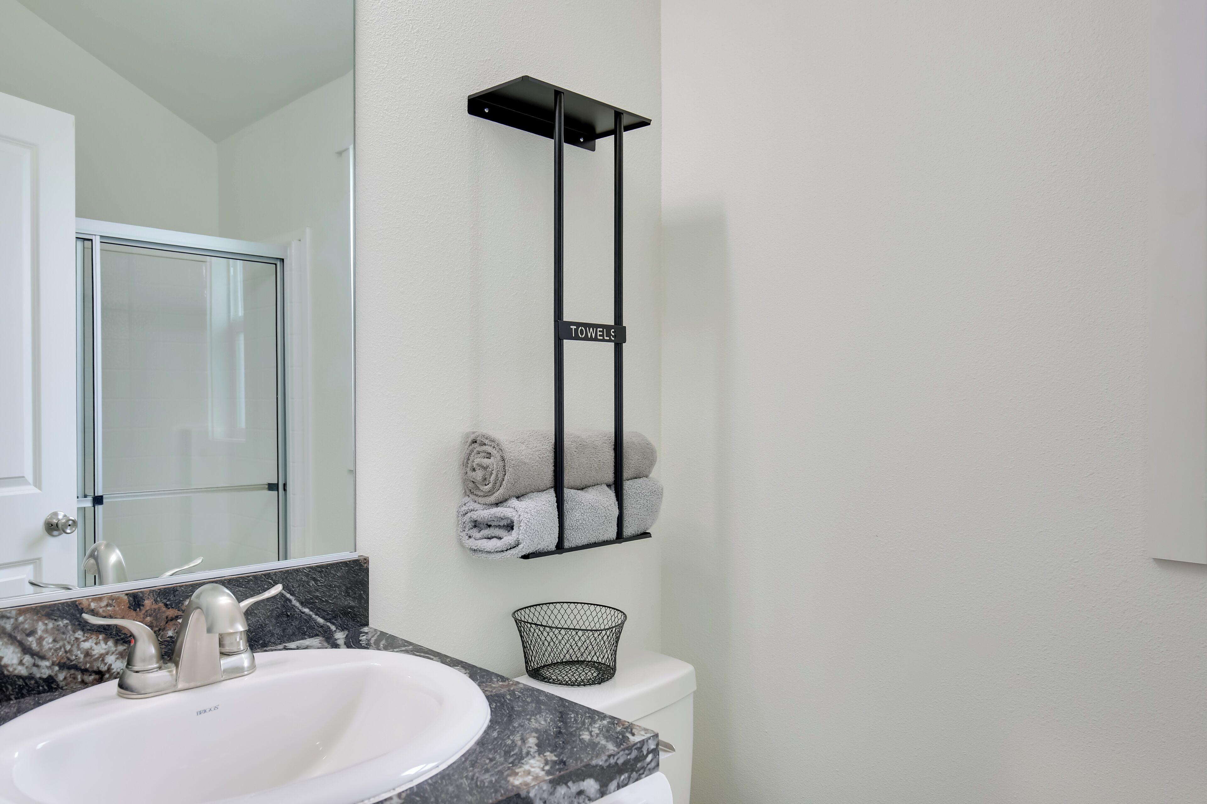 Un baño con un lavamanos blanco, una encimera de mármol, un tozalete negro y una cesta para toallas.
