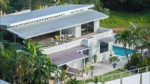 Una casa moderna de dos pisos con techo plano, una piscina y un patio con mobiliario exterior.