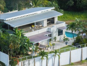 Ein modernes, zweistöckiges Haus mit Flachdach, Swimmingpool und einer Terrasse mit Gartenmöbeln.