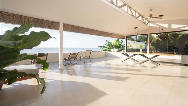 Un balcón amplio con vista al mar, muebles modernos y ventanas grandes.