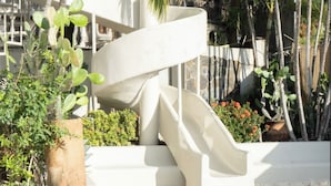 Una escalera en espiral junto a una piscina, rodeada de plantas en macetas y un muro de piedra.