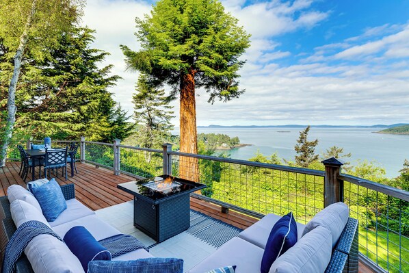 Eine Terrasse mit Sitzgelegenheit im Freien, einer Feuerstelle und Blick auf See und Wald.