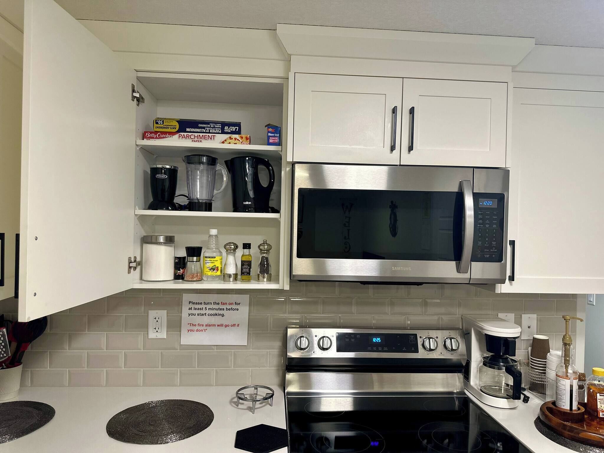 A kitchen with white cabinets, a stainless steel microwave, a stove, and a coffee maker.