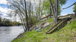 Ein Haus direkt am Flussufer, verbunden durch eine Treppe, umgeben von Bäumen und einer Rasenfläche.