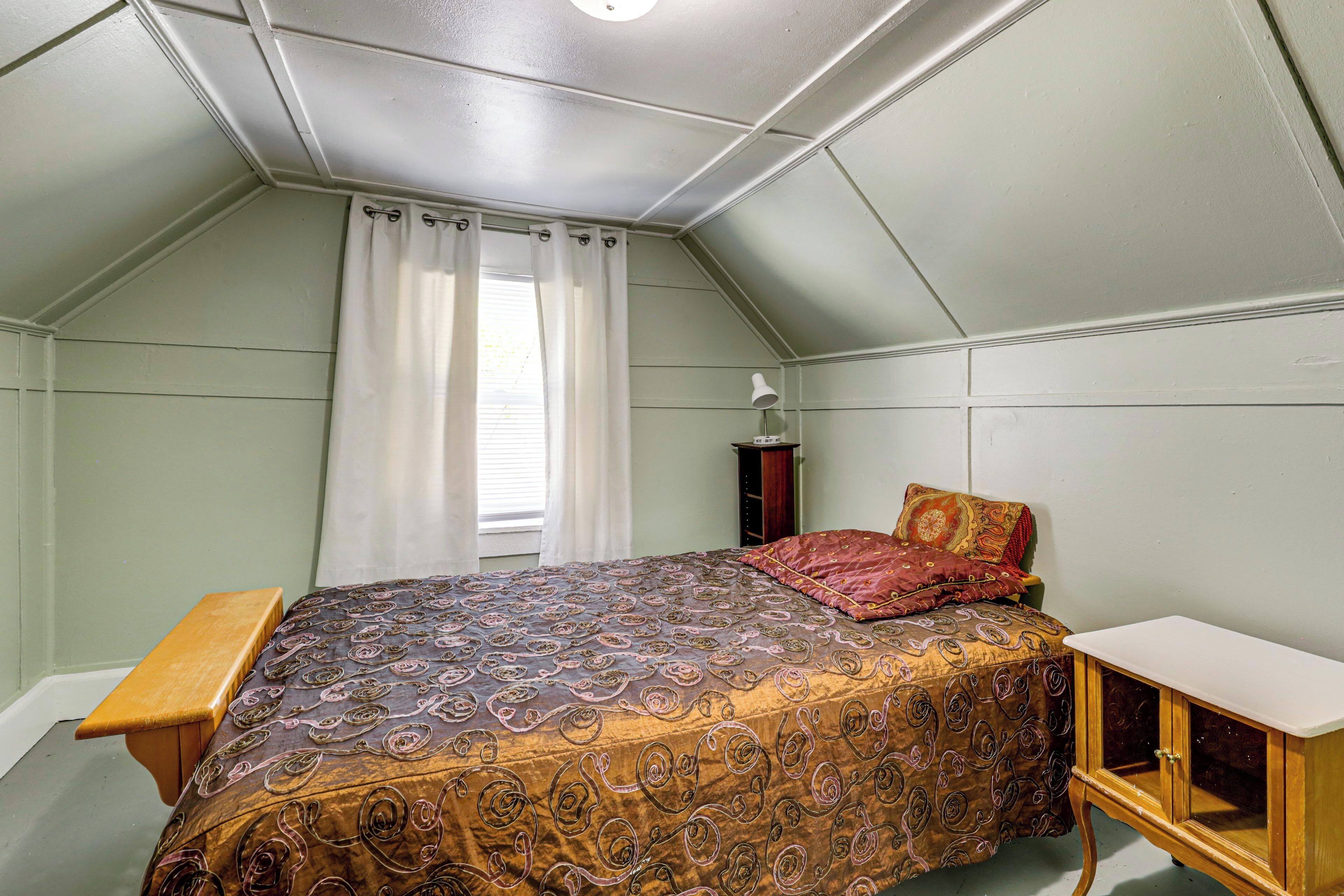 A bedroom with a bed, a nightstand, a lamp, and a window with curtains.