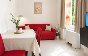 A living room with a red sofa, a dining table with a white tablecloth, a TV, and a window with curtains. - Lovely apartment in Lumbarda with house sea view (Lumbarda)