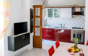 A compact kitchen with a TV, red cabinets, a tiled backsplash, and a dining area with a fruit bowl. - Lovely apartment in Lumbarda with house sea view (Lumbarda)