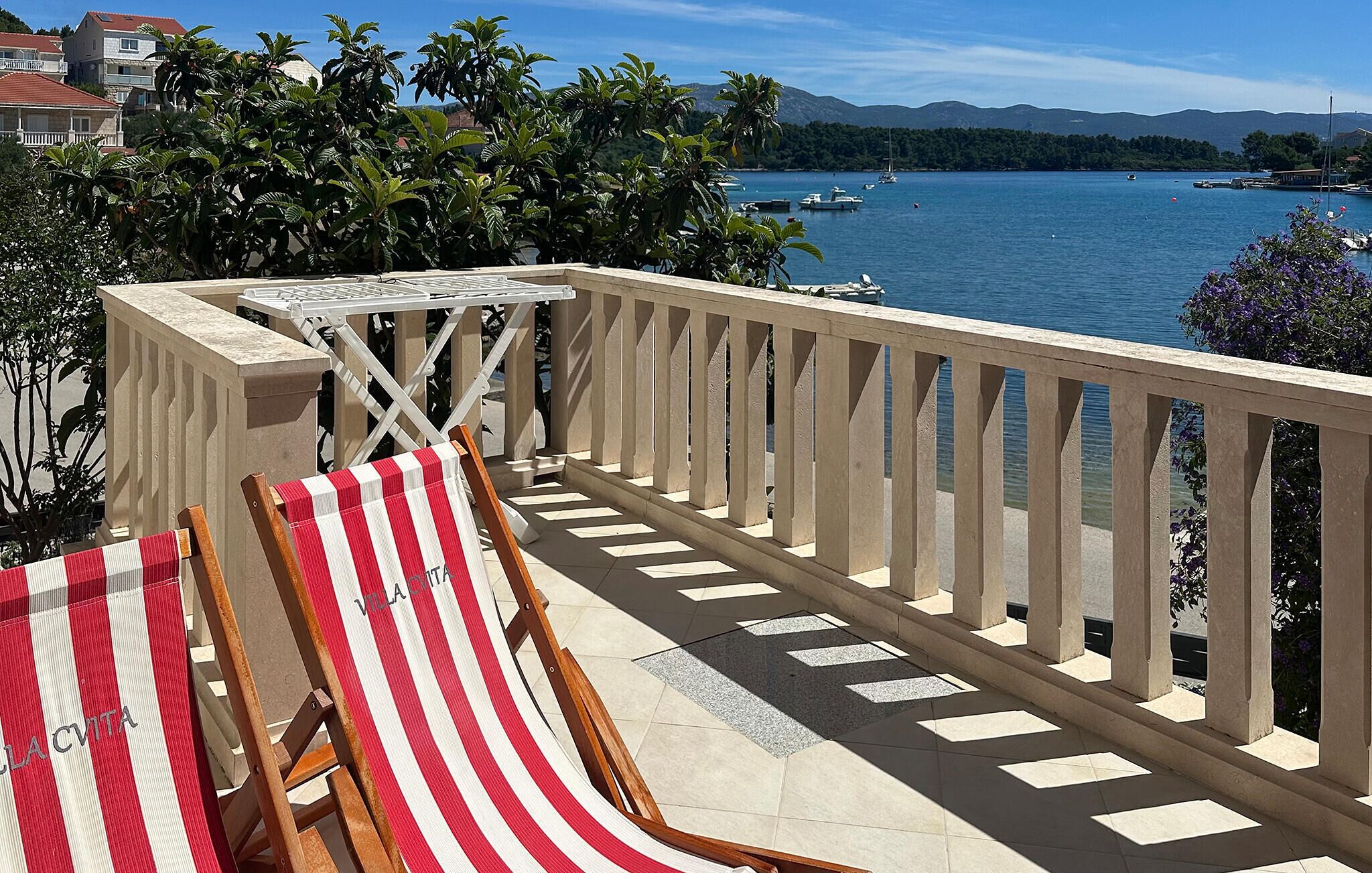 A balcony with a view of a lake, a striped beach chair, and a table.