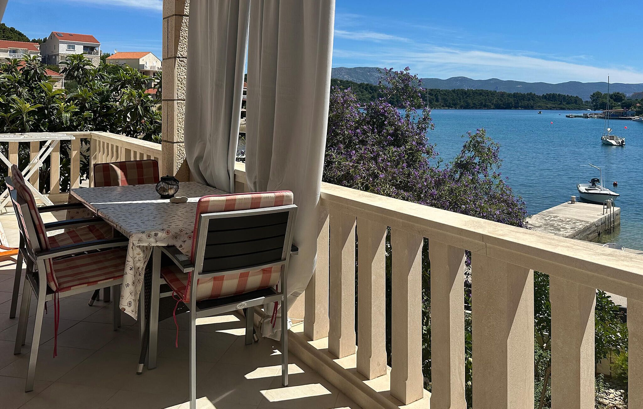 Ein Balkon mit Tisch und Stühlen, mit Blick auf einen See mit Booten und einer Berglandschaft.