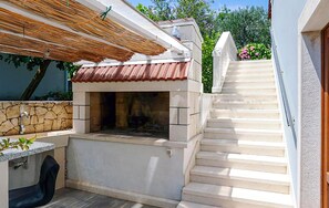 An outdoor kitchen with a stone wall, a grill, and a staircase leading to a second floor. - Lovely apartment in Lumbarda with house sea view (Lumbarda)