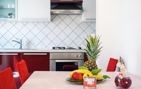 A modern kitchen with a dining table set for two, featuring a fruit platter, a candle, and a glass of red wine. - Lovely apartment in Lumbarda with house sea view (Lumbarda)