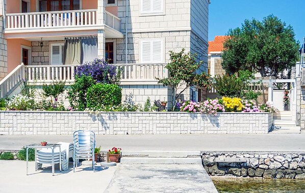Un edificio con balconi, un muro in pietra fiorito e una zona pavimentata con sedie e tavoli.