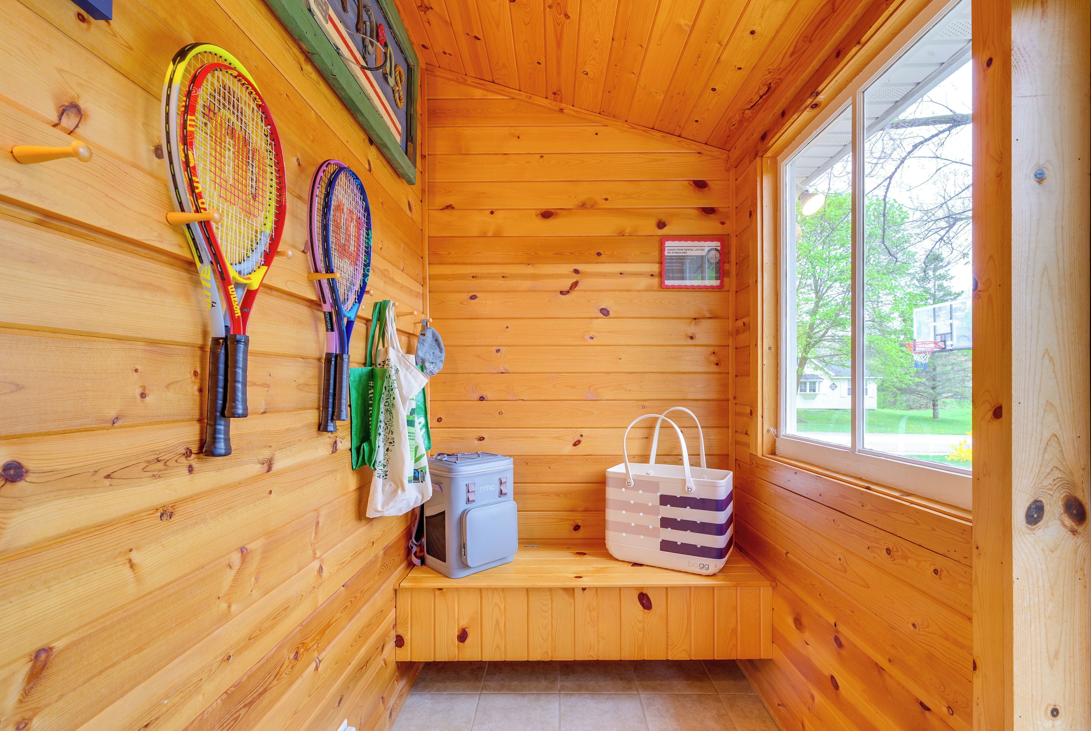 Une cabane en bois avec un banc, deux raquettes de tennis, un sac et un petit radiateur.