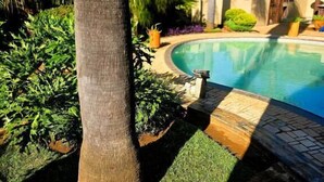 Una piscina rodeada de exuberante vegetación y un sendero de piedra que conduce a un edificio.