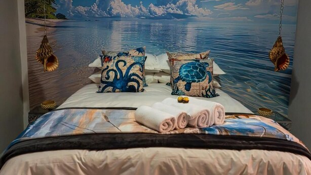 Una cama con vista a una playa y al océano a través de un ventanal grande.