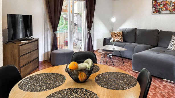 Uma sala de estar moderna com sofá, TV, mesa de jantar e vista para o exterior.