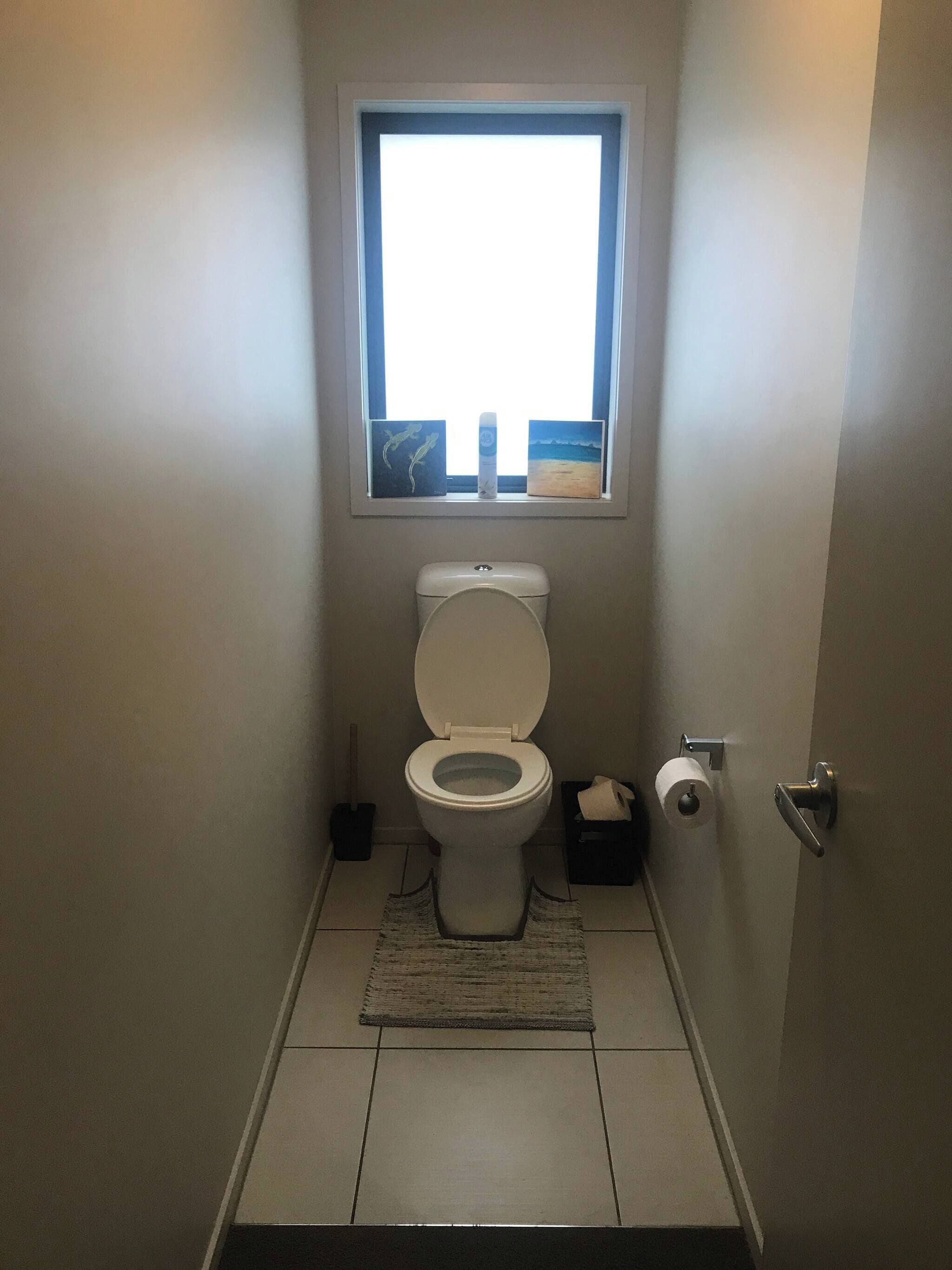 Un baño pequeño con inodoro, ventana y alfombra.