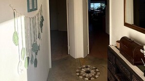 Un couloir orné d’un élément décoratif fixé au mur, une porte donnant sur une autre pièce et un banc avec un miroir.