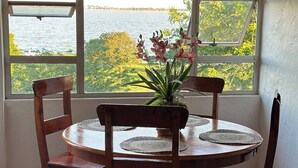Un coin repas avec une table ronde, quatre chaises, une plante en pot et une vue sur une étendue d’eau grâce à de grandes fenêtres.