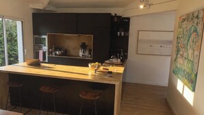 A modern kitchen with a central island, bar stools, a dining table, and a yellow rug. - Villa with pool near Hossegor beaches (Angresse)