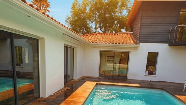 A swimming pool with wooden decking, a glass door entrance, and a building with a tiled roof. - Villa with pool near Hossegor beaches (Angresse)