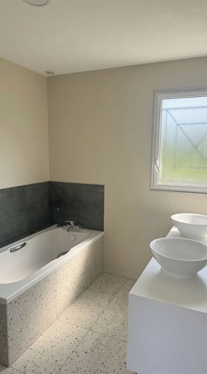 Ein Badezimmer mit einer Badewanne, einem Fenster und einem Waschtisch mit einer Waschschüssel.