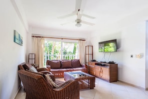Ein Wohnzimmer mit einer Couch, Sesseln, einem Couchtisch, einem Fernseher und einem Deckenventilator.