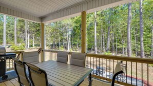 Eine überdachte Terrasse mit Tisch und Stühlen, umgeben von einem Holzgeländer und Blick auf ein bewaldetes Gebiet.