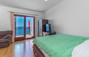 Ein Schlafzimmer mit einem grünen Bett, einer Couch, einem Fernseher und einem Balkon mit einem roten Sonnenschirm.