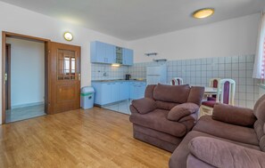 Ein Wohnzimmer mit einer Couch, einer Holztür, einem Mülleimer und einer Küchenzeile mit Schränken und einer gefliesten Rückwand.