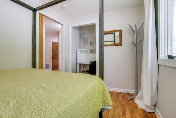 Ein Schlafzimmer mit Bett, Schreibtisch, Stuhl, Kleiderhaken und einem Fenster mit Vorhängen.