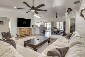 A spacious living room with a large flat-screen TV, a ceiling fan, and a dining area with a kitchen in the background. - Outdoor Entertainment! Extended Lake Havasu Escape (Lake Havasu City)