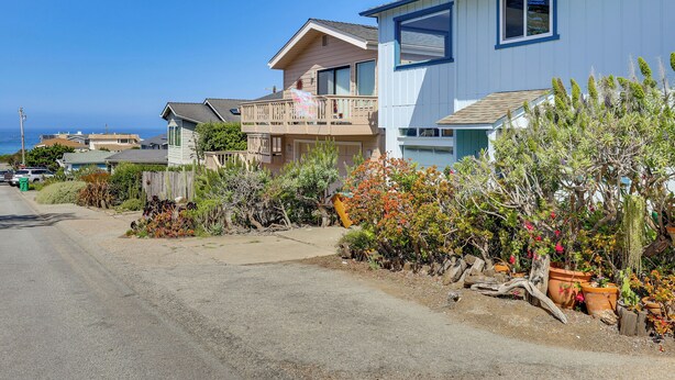 A residential street with houses, a clear sky, and a view of the ocean.