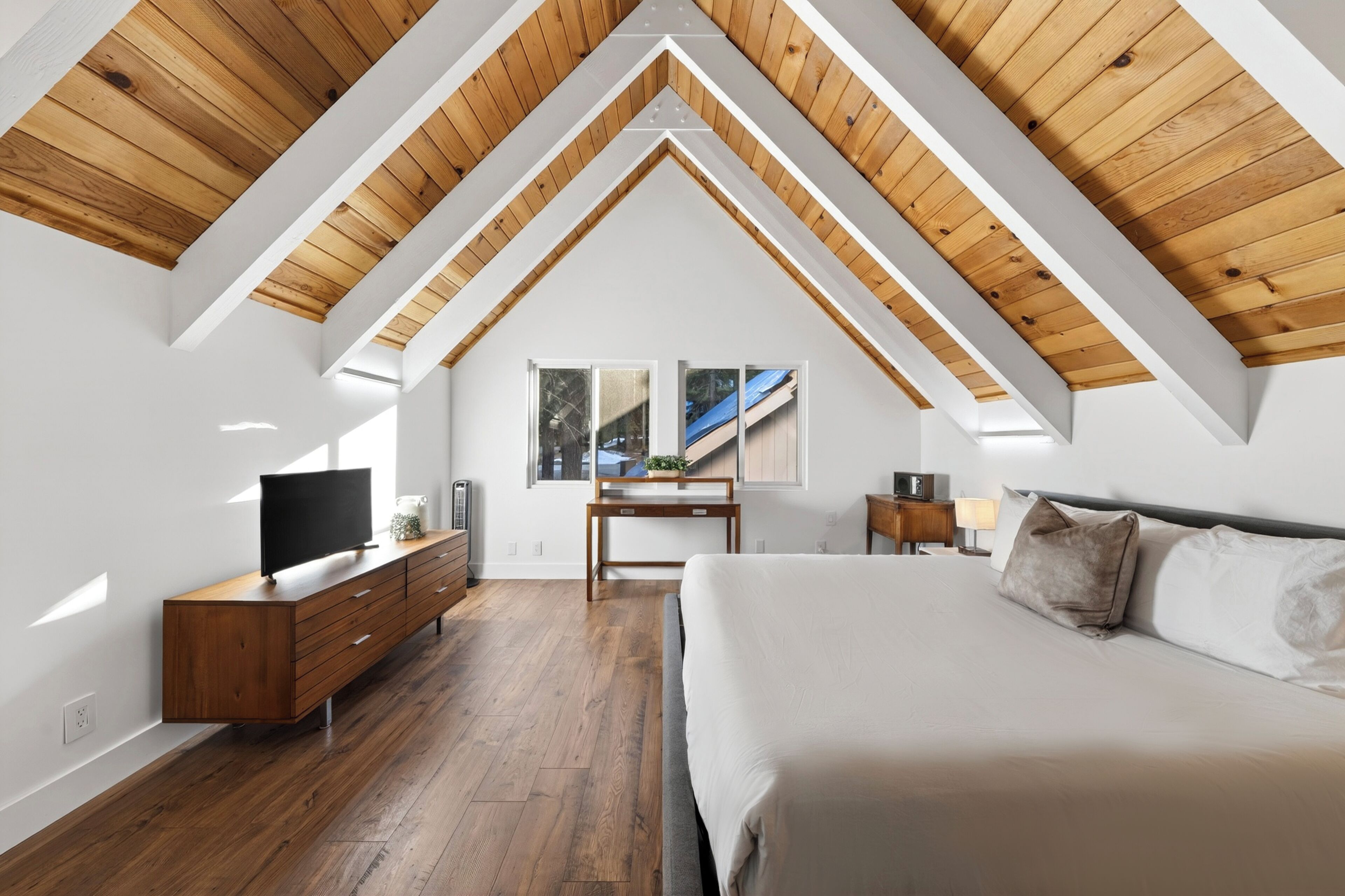 A bedroom with a wooden ceiling, a bed, a TV, a desk, and a window.