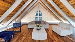 Ein Dachzimmer mit Holzbalkendecke, einer Couch, einem Couchtisch und Blick durch ein Fenster.