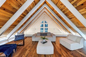 Ein Dachzimmer mit Holzbalkendecke, einer Couch, einem Couchtisch und Blick durch ein Fenster.