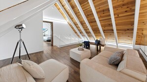 Ein modernes Schlafzimmer im Loft-Stil mit schrägem Dach, Holzbalken, einem großen Fenster und einer gemütlichen Sitzecke mit Kissen.